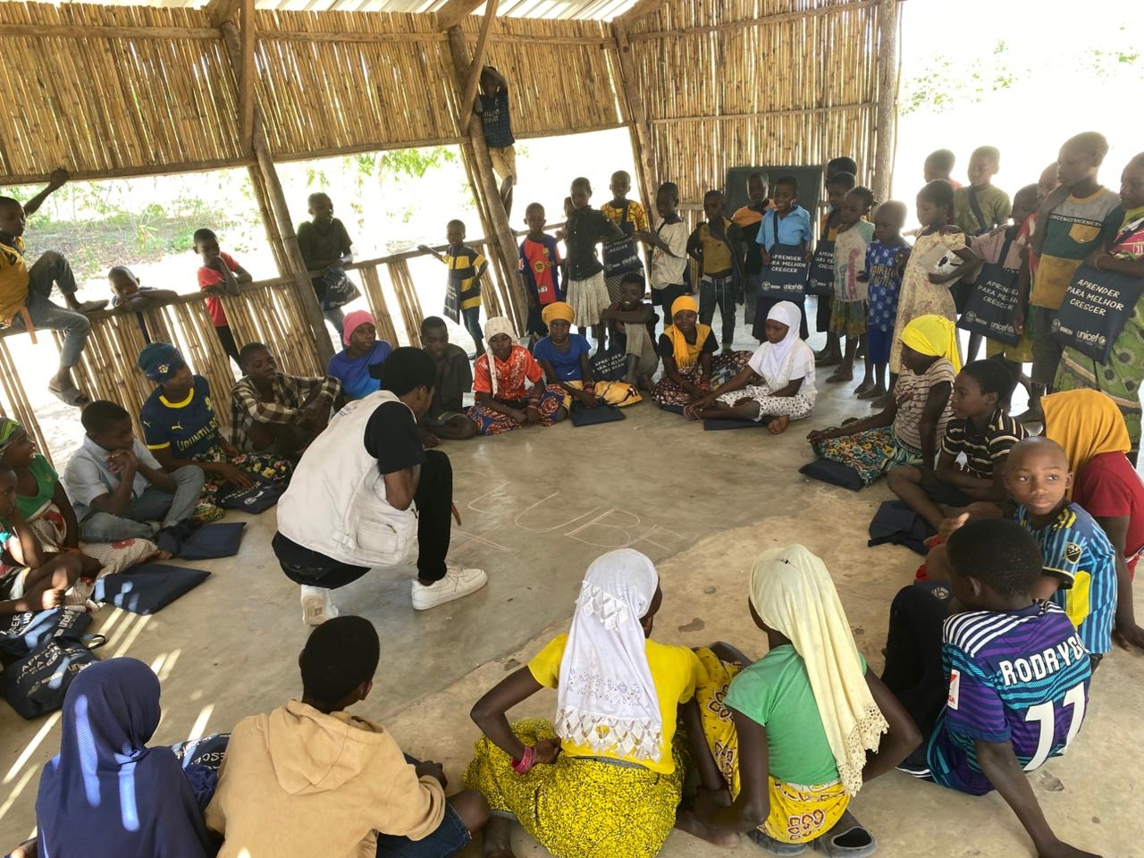 Barn sitter i en ring på golvet medan en manlig lärare ritar på golvet i mitten.