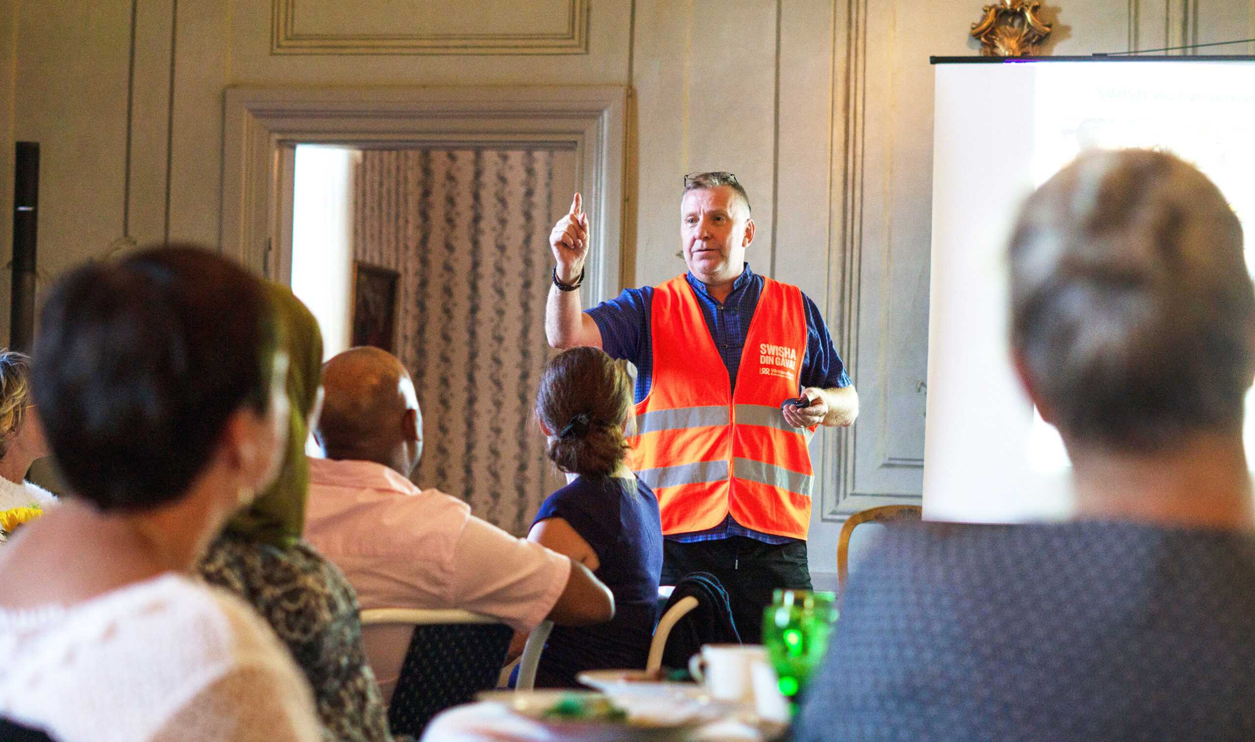 Man i VärldensBarn väst står och pratar framför en grupp sittande människor.