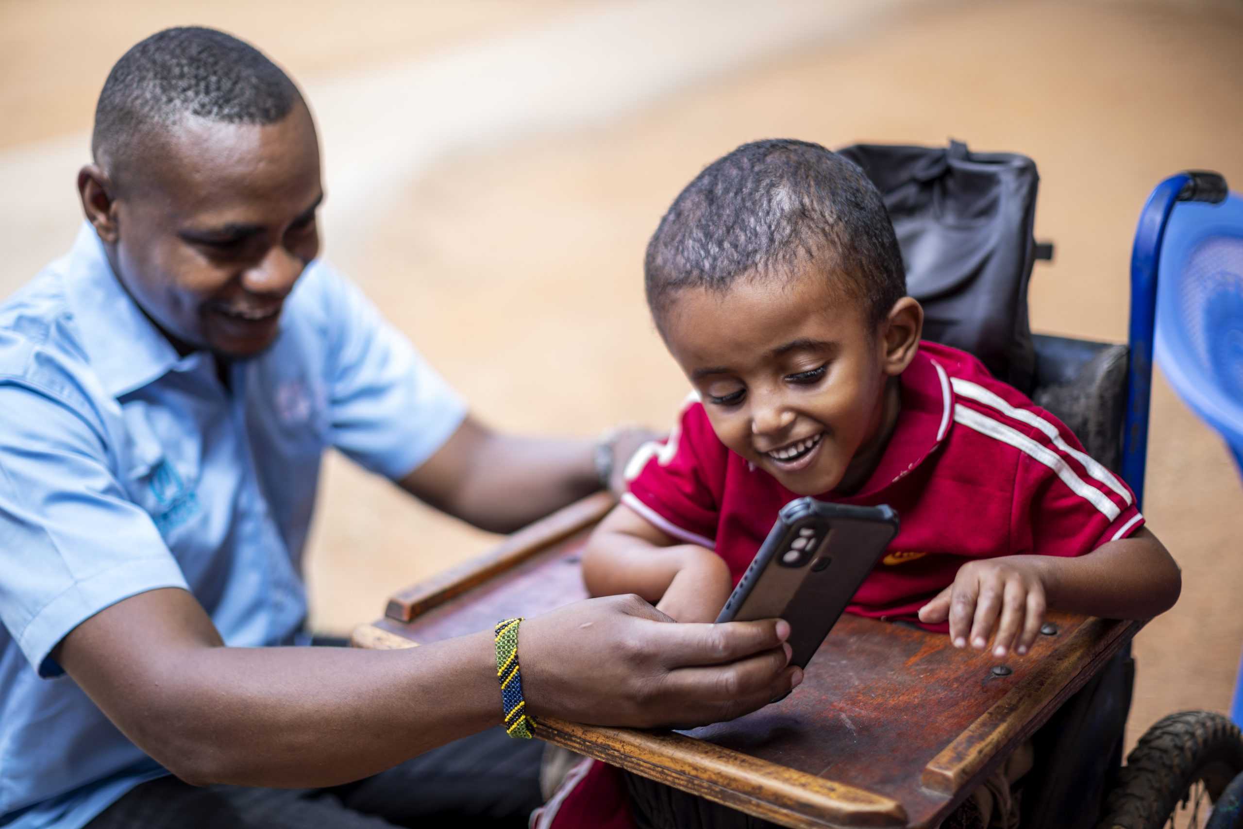 En man visar en mobiltelefon för ett barn. Båda skrattar.